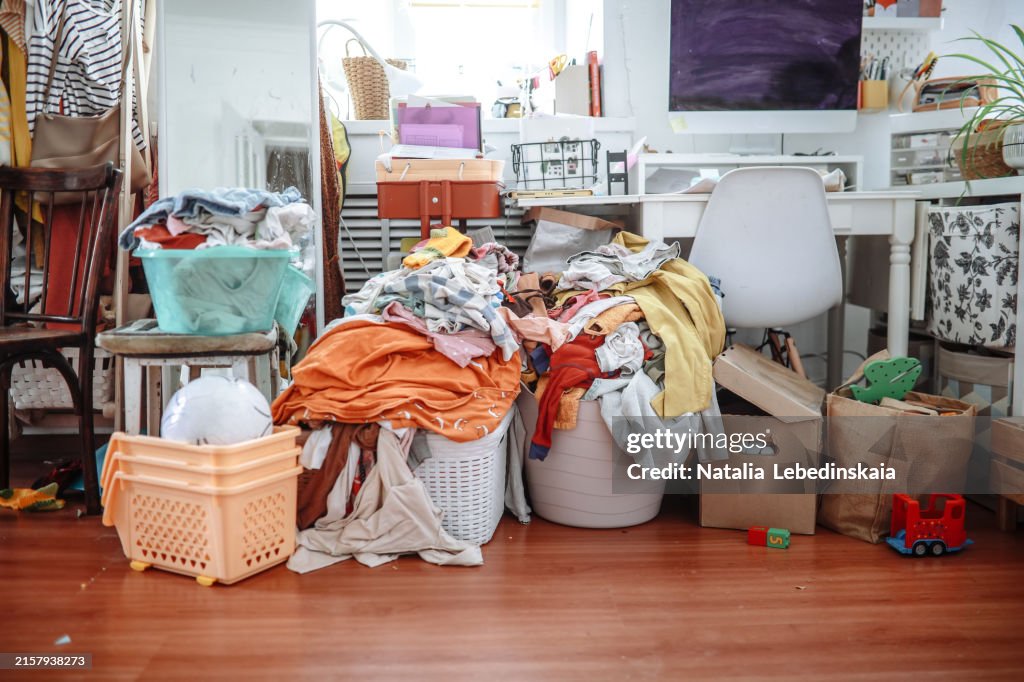 Household chaos: baskets of clean laundry and huge piles of clothes in cluttered living room
