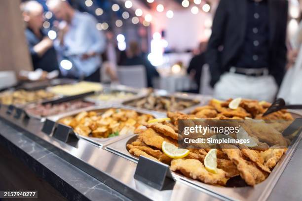 a buffet table full of different types of meat, fish and salads. unrecognizable caucasian men, wedding or reception guests scooping up food. - produit à base de viande photos et images de collection