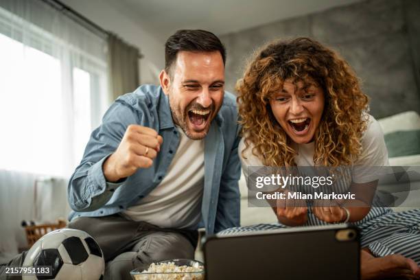 couple watching soccer match together on digital tablet at home - titta på bildbanksfoton och bilder