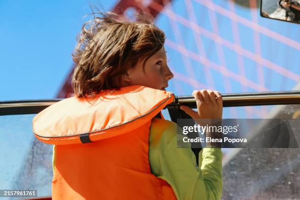 rear view curious 10 years old boy wearing orange life jacket for safety traveling on motor boat - 10 11 years stock pictures, royalty-free photos & images