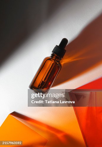 Amber Glass Dropper Bottle of Skincare Product Casting Illuminating Shadows Under the Sunlight on White Background. Beauty, Wellness, Vitality Amber Glass Dropper Bottle of Skincare Product Casting Illuminating Shadows Under the Sunlight on White Background. Beauty, Wellness, Vitality