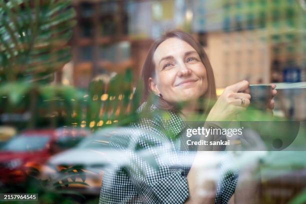satisfied woman in cafe with cup of hot coffee. photographed through window - view-through-restaurant-window stock pictures, royalty-free photos & images