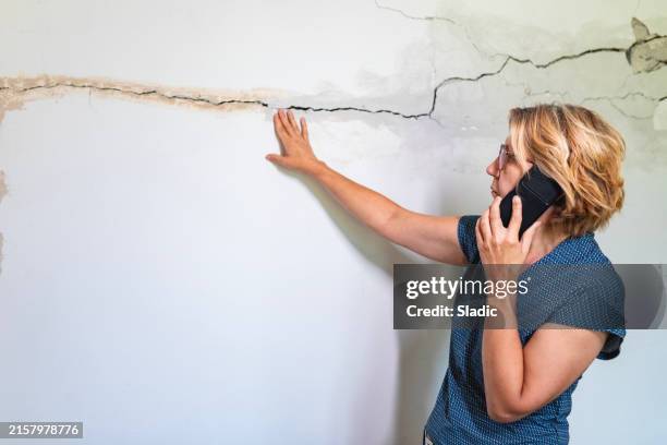 woman looking at a wall damaged after the earthquake - aardbeving stockfoto's en -beelden