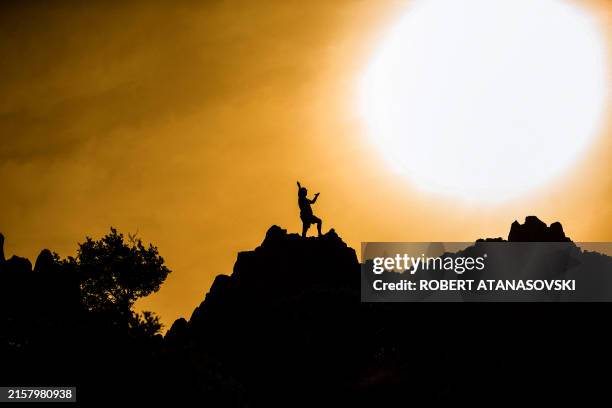 Man is silhouetted standing on the rocky crest filled with astronomical markers at the megalithic observatory on the day of the Summer solstice, in...