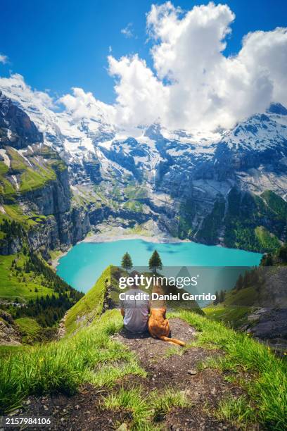 owner and his dog contemplating the spectacular landscape of the swiss alps, owner and his dog contemplating the lake and the mountains. - lac-oeschinensee photos et images de collection