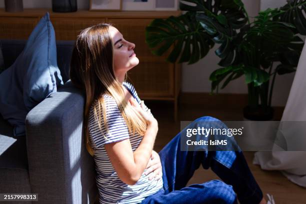 woman is enjoying sunlight and meditating in her living room - exhaling stock pictures, royalty-free photos & images