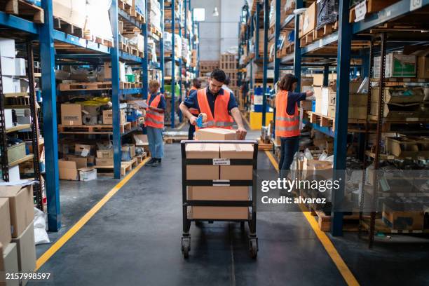 ouvrier emballant une boîte en carton avec du ruban adhésif sur le chariot de l’entrepôt de distribution - chariot photos et images de collection