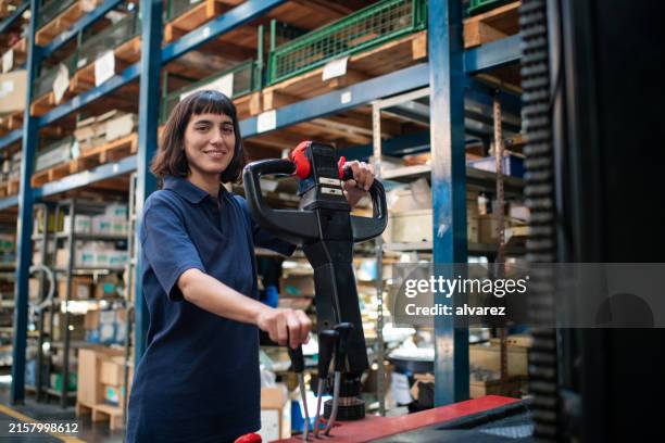 mujer joven operando una transpaleta eléctrica de montacargas en el almacén - carretilla elevadora fotografías e imágenes de stock