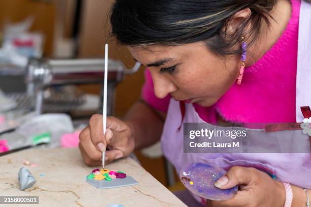 craftwoman concentrating on decorating small clay figurines with colorful enamel - enamel jewellery stock pictures, royalty-free photos & images