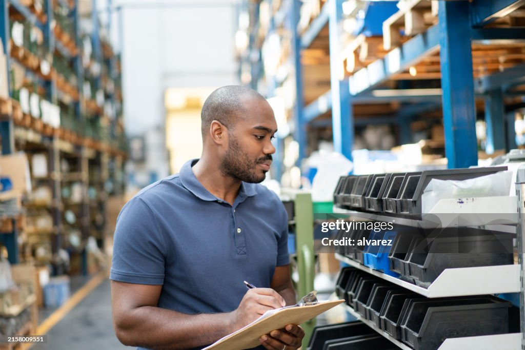African worker managing inventory with clipboard in distribution center