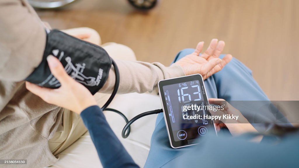Close up woman caregiver nurse wearing blue scrubs checks blood pressure monitor and heart rate monitor with digital pressure gauge to elderly woman retirement sitting on bed in bedroom,healthcare setting medical health care plan