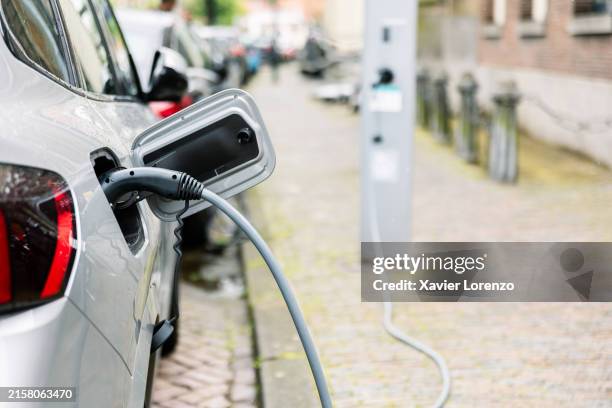 electric car charging through plug on street. - elektrische auto stockfoto's en -beelden