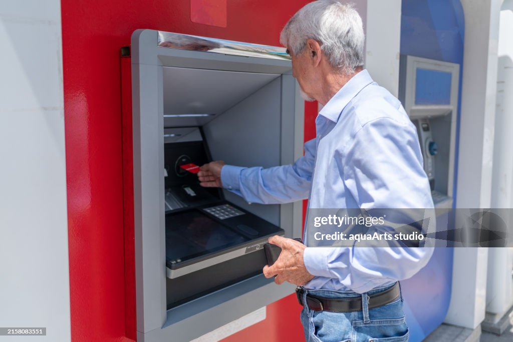 屋外ATMにクレジットカードを挿入する年配の男性