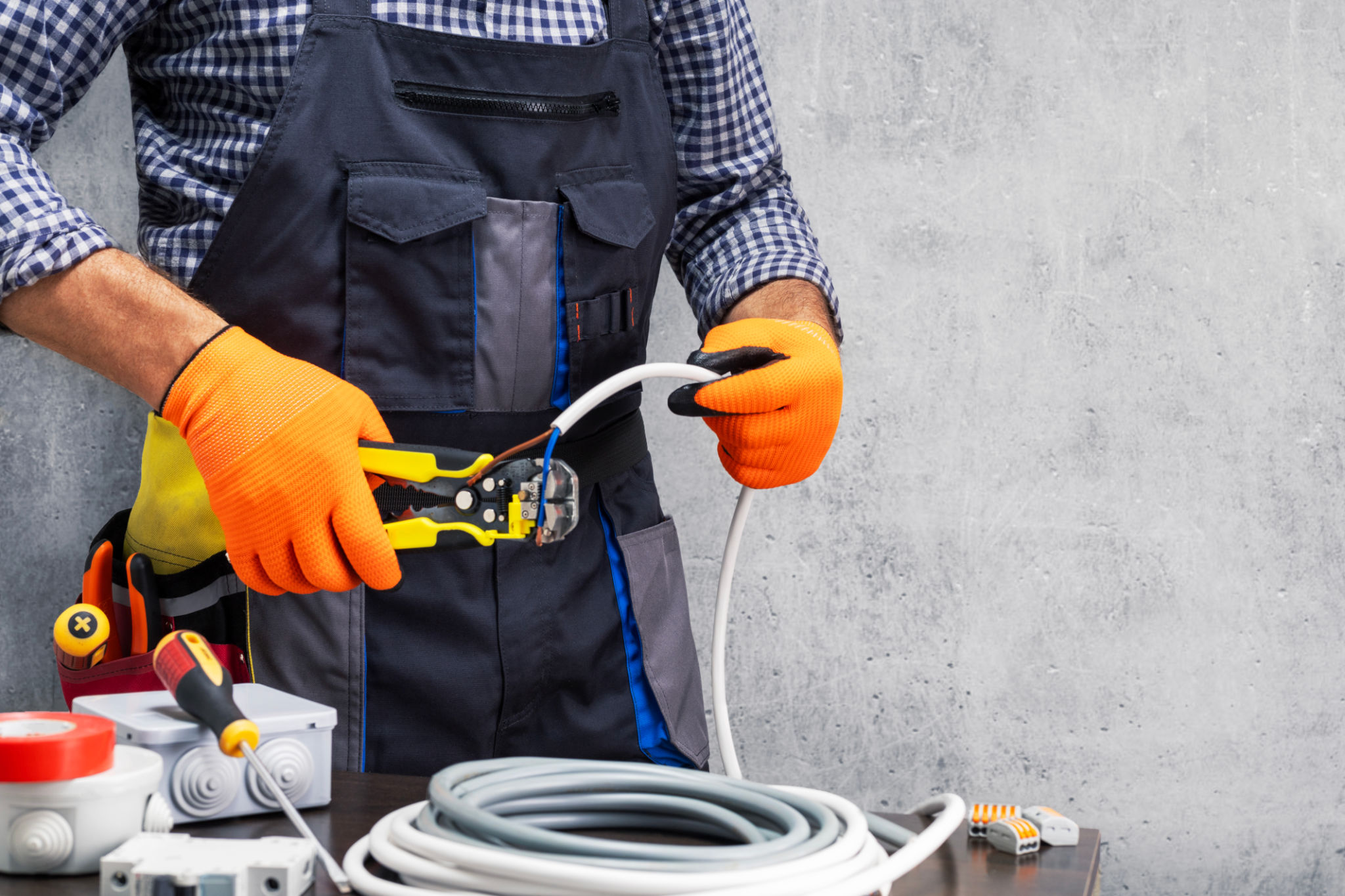 electrician worker striping the insulation of wires. electrician working against concrete wall. electrician worker striping the insulation of wires. electrician working against concrete wall.