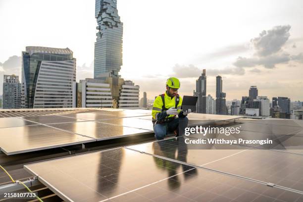 rooftop worker uses solar-powered laptop on tall building. - tour structure bâtie photos et images de collection