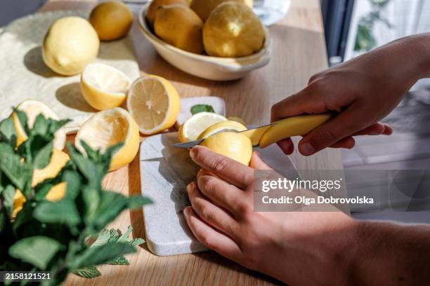 hands cutting a lemon on a chopping board - lemon fruit stock pictures, royalty-free photos & images