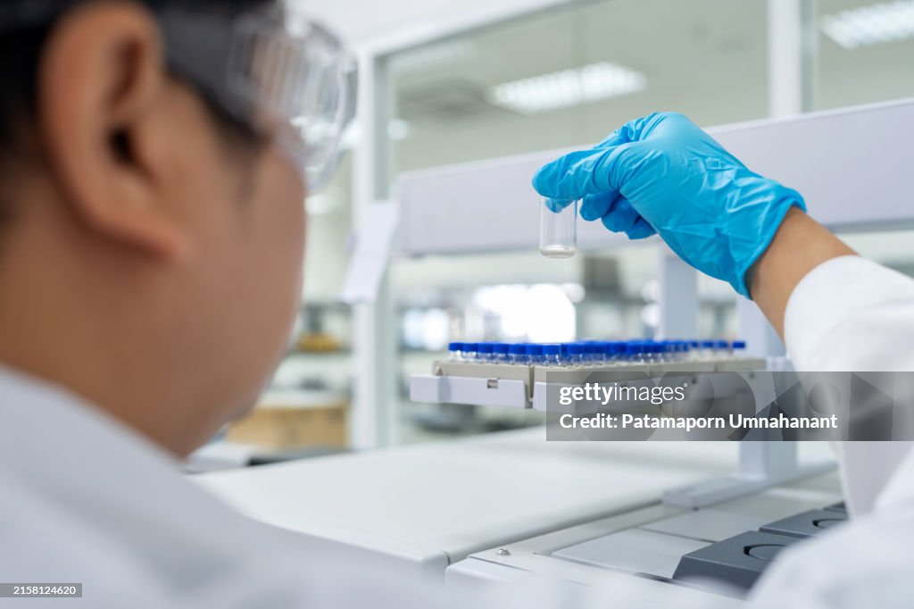 Científico realizando análisis con GC-MS en laboratorio. Toma un vial de muestra y lo coloca cuidadosamente en la bandeja del equipo GC-MS para analizar la composición de la muestra.