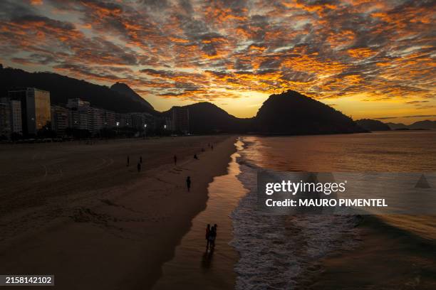 People walk during sunrise ahead of an open-air yoga session at Copacabana beach in Rio de Janeiro on June 22, 2024.