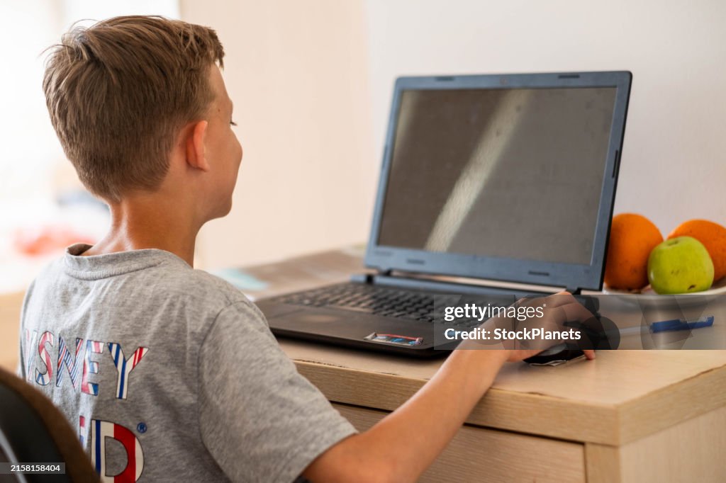 Rückansicht eines Jungen, der an einem Tisch sitzt und einen Laptop benutzt