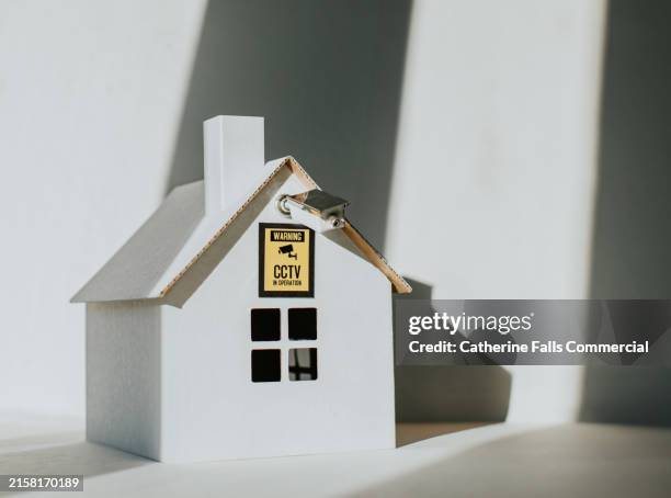 conceptual image of a small, cardboard house with a security camera mounted on the wall - burglar alarm stock pictures, royalty-free photos & images