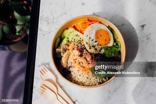 healthy food bowl with shrimps, brown rice, fried egg, lettuce and vegetables in disposable eco-friendly packaging. high angle view, flat lay - brown rice stock pictures, royalty-free photos & images
