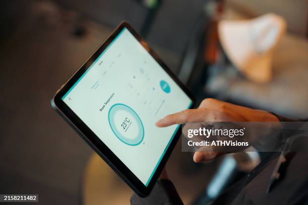 hostel staff use digital tablet to check and adjust temperature settings in a modern, stylish interior with ambient lighting - thermostaat stockfoto's en -beelden