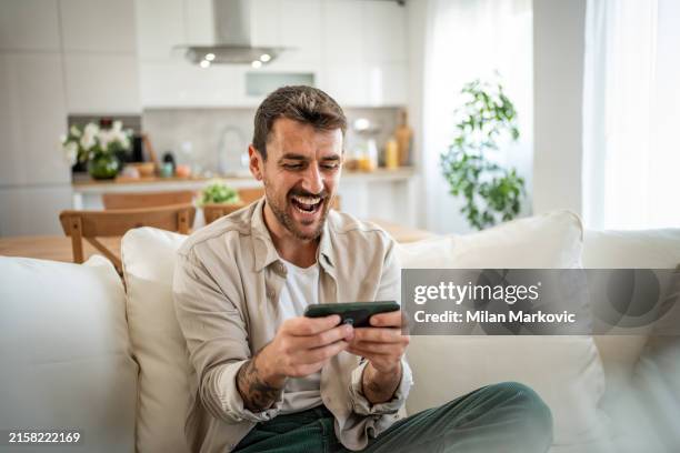 a young man spends time playing smatphone games in his new home - homens de idade mediana imagens e fotografias de stock
