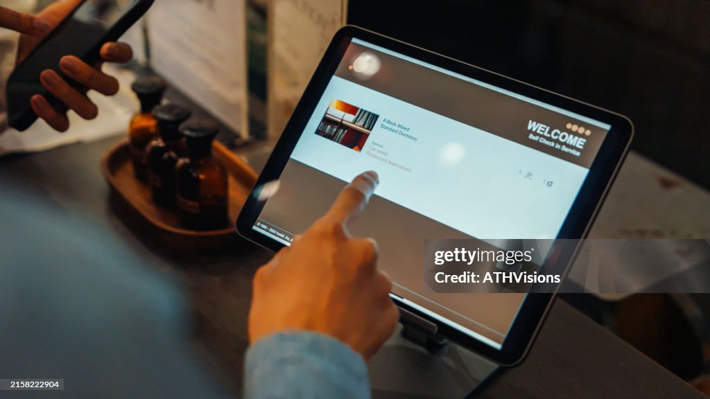 A guest uses a self check-in kiosk at a hostel, selecting room options on a tablet. The process is streamlined and efficient.