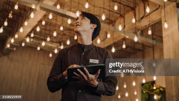 hostel staff use digital tablet to check and adjust energy in a modern, stylish interior with ambient lighting - hotel receptionist man stock pictures, royalty-free photos & images