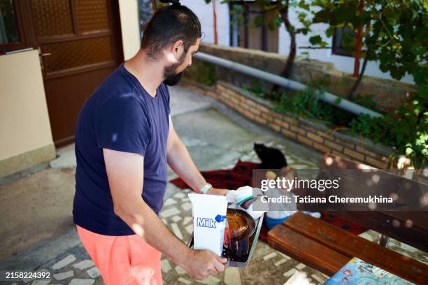 a middle-aged man clears away dishes after eating in the courtyard. his little son is playing nearby. - drudgery stock pictures, royalty-free photos & images