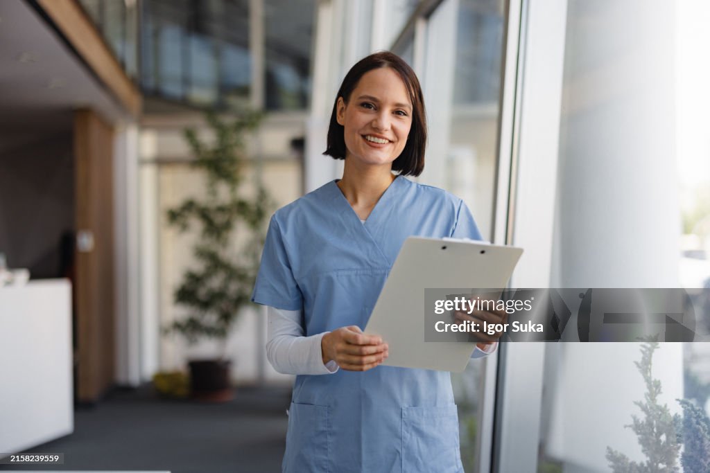 Smiling Medical Professional in Scrubs Holding a Clipboard in Hospital Setting