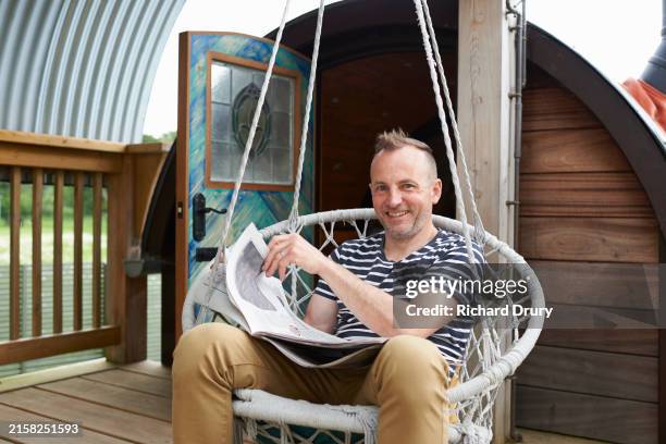 a gay man sitting in a swinging chair and holding a newspaper - non moving activity stock pictures, royalty-free photos & images