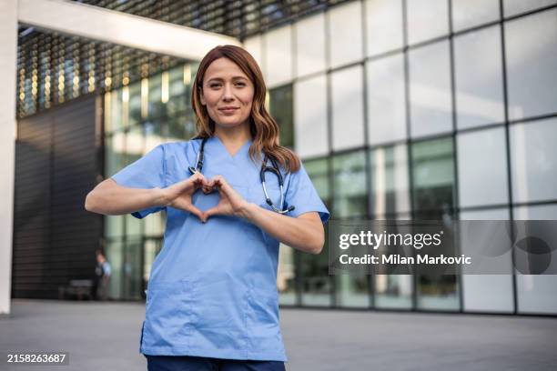 heart of health - female medical worker posing in front of the hospital, showing a heart with her fingers - images love hearts stock pictures, royalty-free photos & images