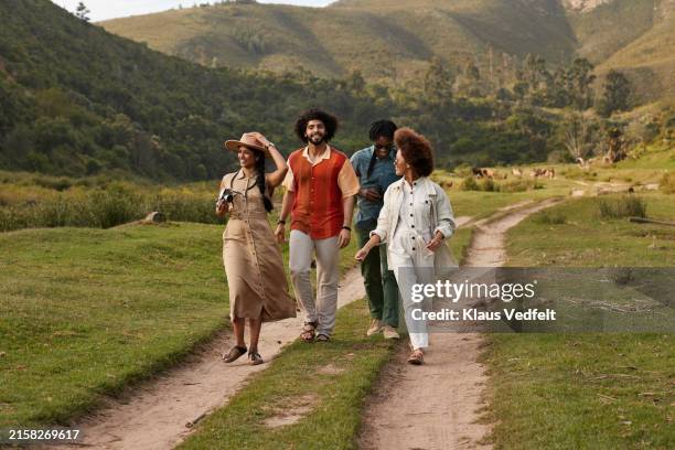 smiling young multiracial friends walking on dirt road - om zich heen kijken stockfoto's en -beelden