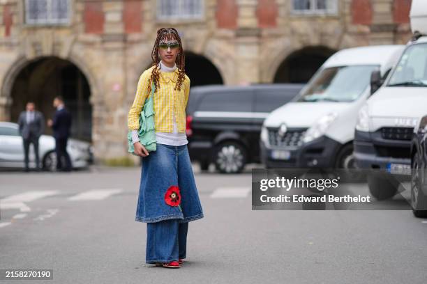 Caroline Takrarit wears green sunglasses, white sheer mesh turtleneck long sleeve shirt, yellow with white lined/pattern button up long sleeve shirt,...