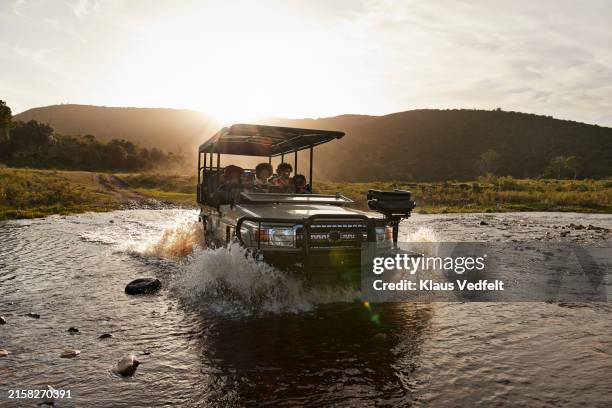 driver and tourists in safari vehicle splashing water in river - safari stockfoto's en -beelden