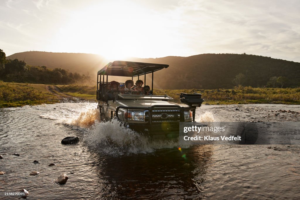 Driver and tourists in safari vehicle splashing water in river