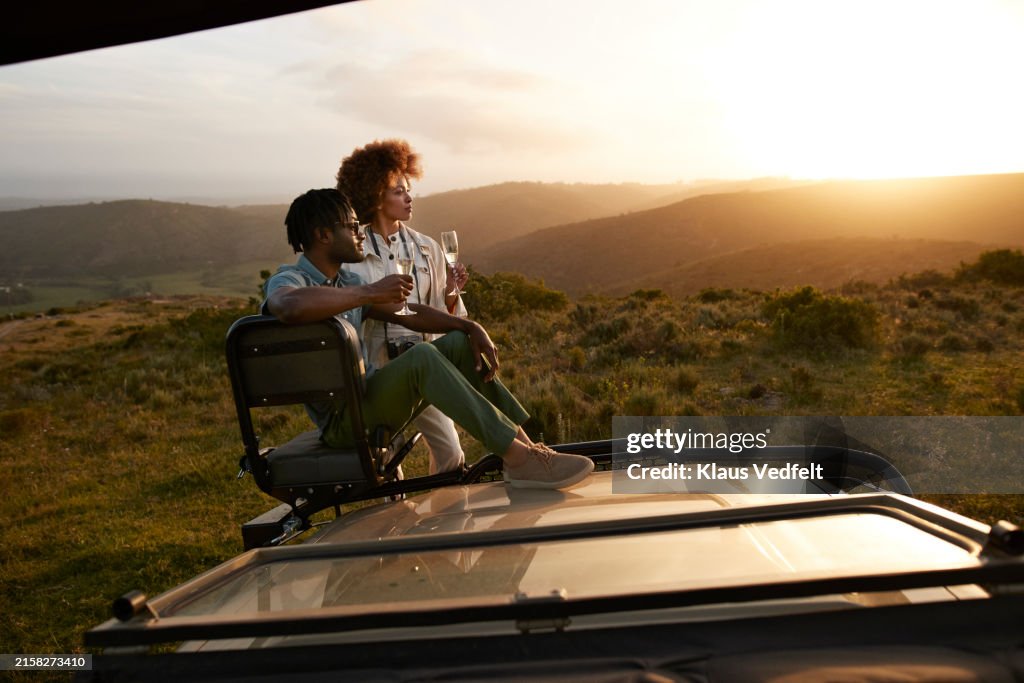 Young couple with champagne flutes on off-road safari vehicle