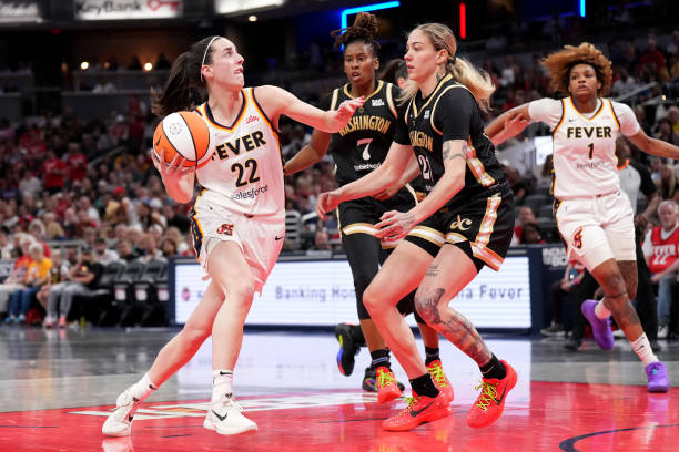 Caitlin Clark of the Indiana Fever drives to the basket against Ariel Atkins and Emily Engstler of the Washington Mystics during the first half of a...