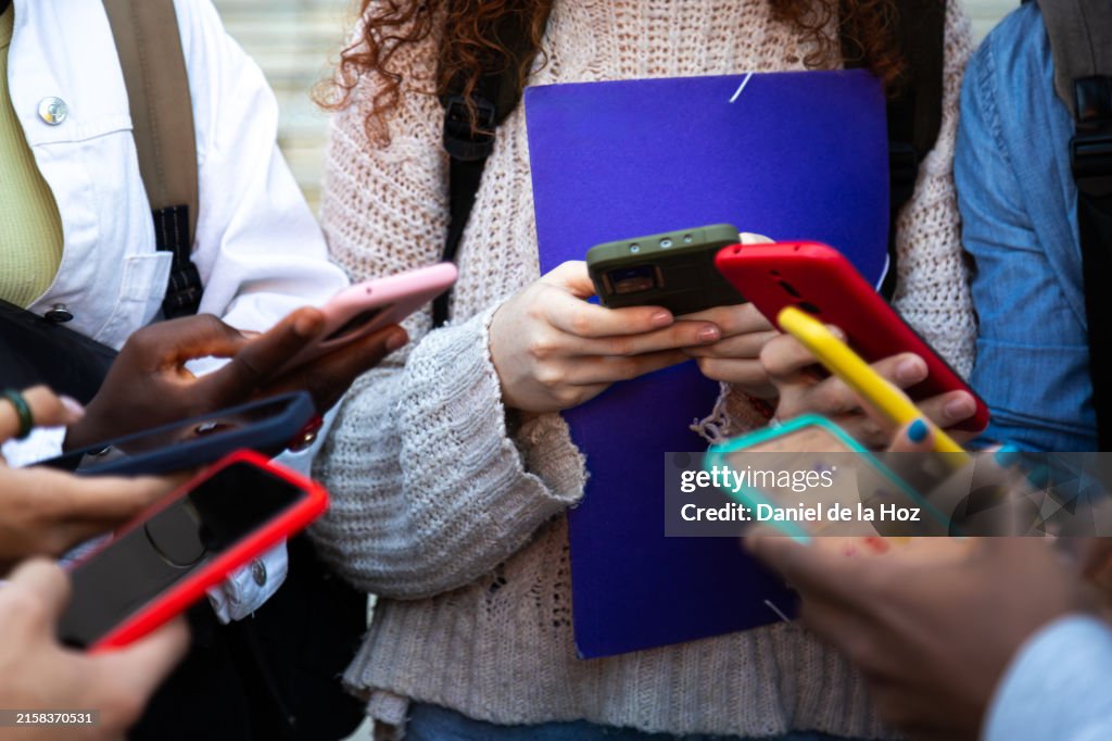 Close up of young college students hands holding mobile phones. Teenagers addicted to smartphones and technology. Group of friends sharing content on social media.