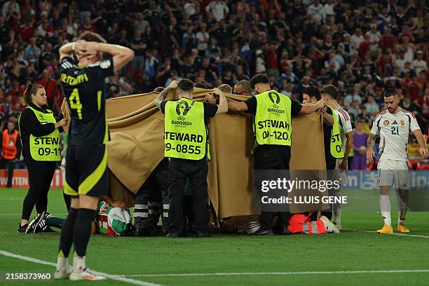 Hungary's forward Barnabas Varga, hidden behind a cloth, receives medical treatment during the UEFA Euro 2024 Group A football match between Scotland...