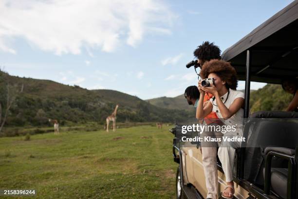 young woman photographing while man looking through binoculars - safari stockfoto's en -beelden