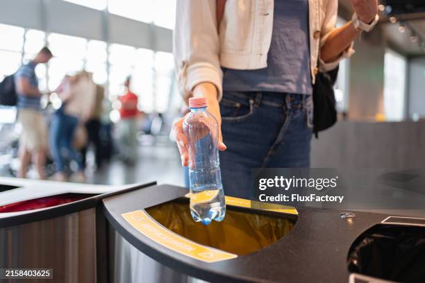 eine verantwortungsbewusste junge frau, die eine plastikflasche in den mülleimer am flughafen wirft - mülltonne stock-fotos und bilder