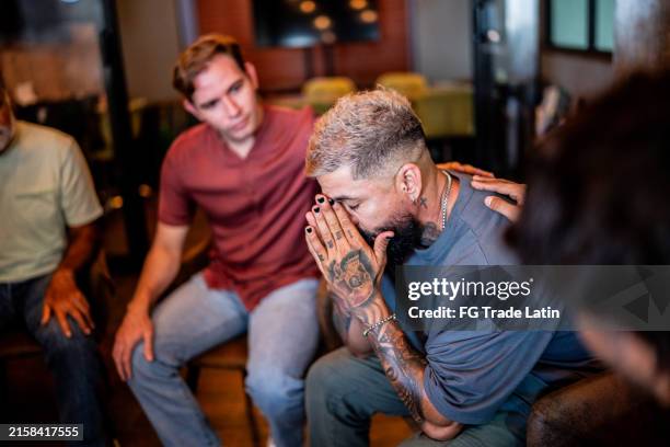 hombre maduro siendo consolado en una terapia de grupo en un centro de salud mental - esclavitud fotografías e imágenes de stock