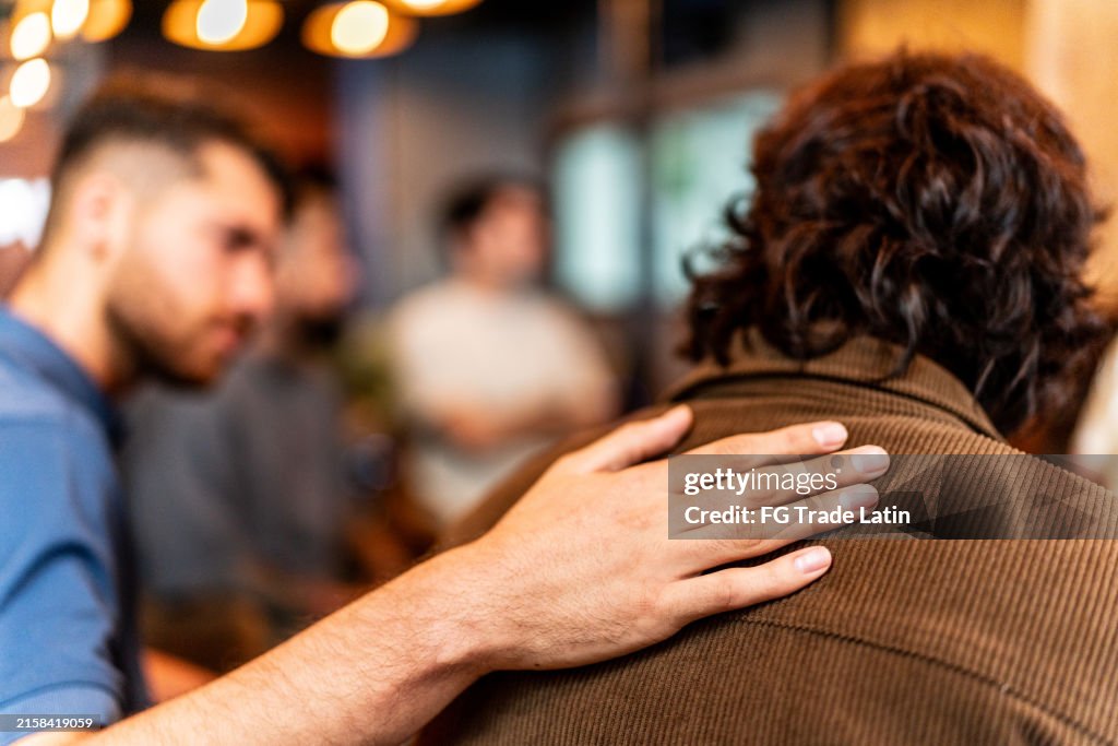 Close-up of man's hand on patient shoulder on a males group therapy at mental health center