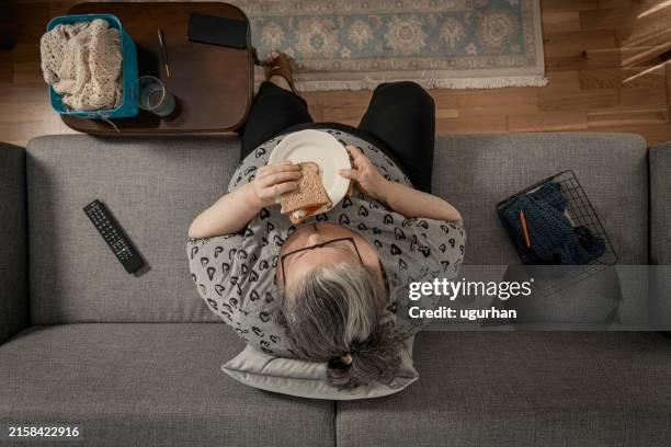 overweight woman eats sandwich on the sofa. - ongezond-leven stockfoto's en -beelden