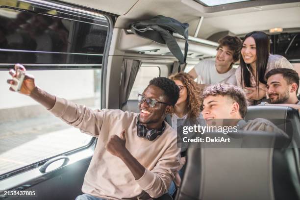 cheerful young black man holding phone and taking selfie picture with his friends. they travel by bus on a joint trip - holiday event stock pictures, royalty-free photos & images