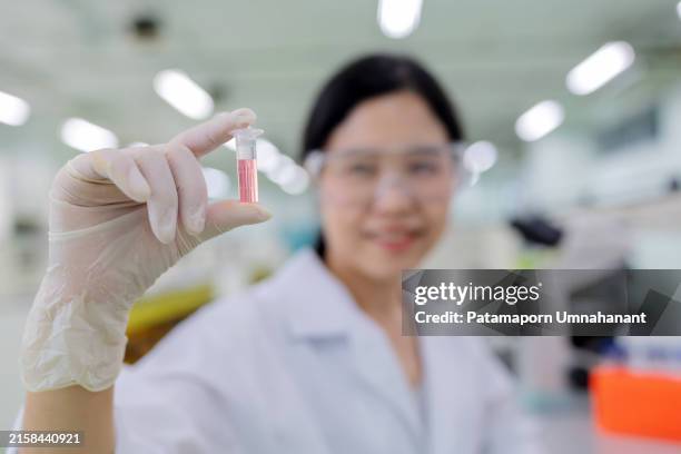 close-up of a scientist's hand holding a sample vial containing a pink solution, showcasing meticulous examination in a modern laboratory. the scientist, donned in protective gloves and lab coat, focuses intently on the sample - test tube stock pictures, royalty-free photos & images