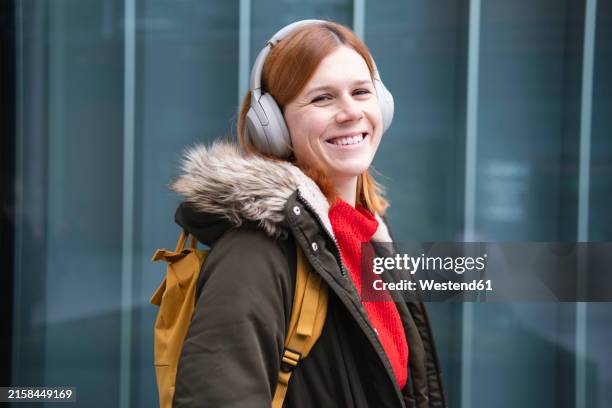 happy redhead woman listening to music through wireless headphones - fur jacket stock pictures, royalty-free photos & images