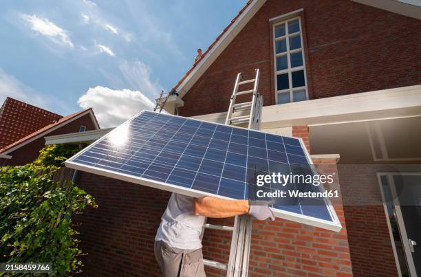 engineer climbing on ladder with solar panel near house - zonnepanelen stockfoto's en -beelden